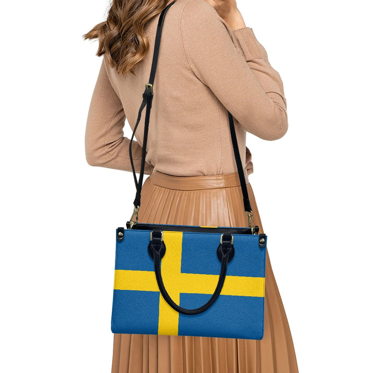woman wearing a tan sweater and pleated skirt carrying a handbag with the Swedish flag design in blue and yellow