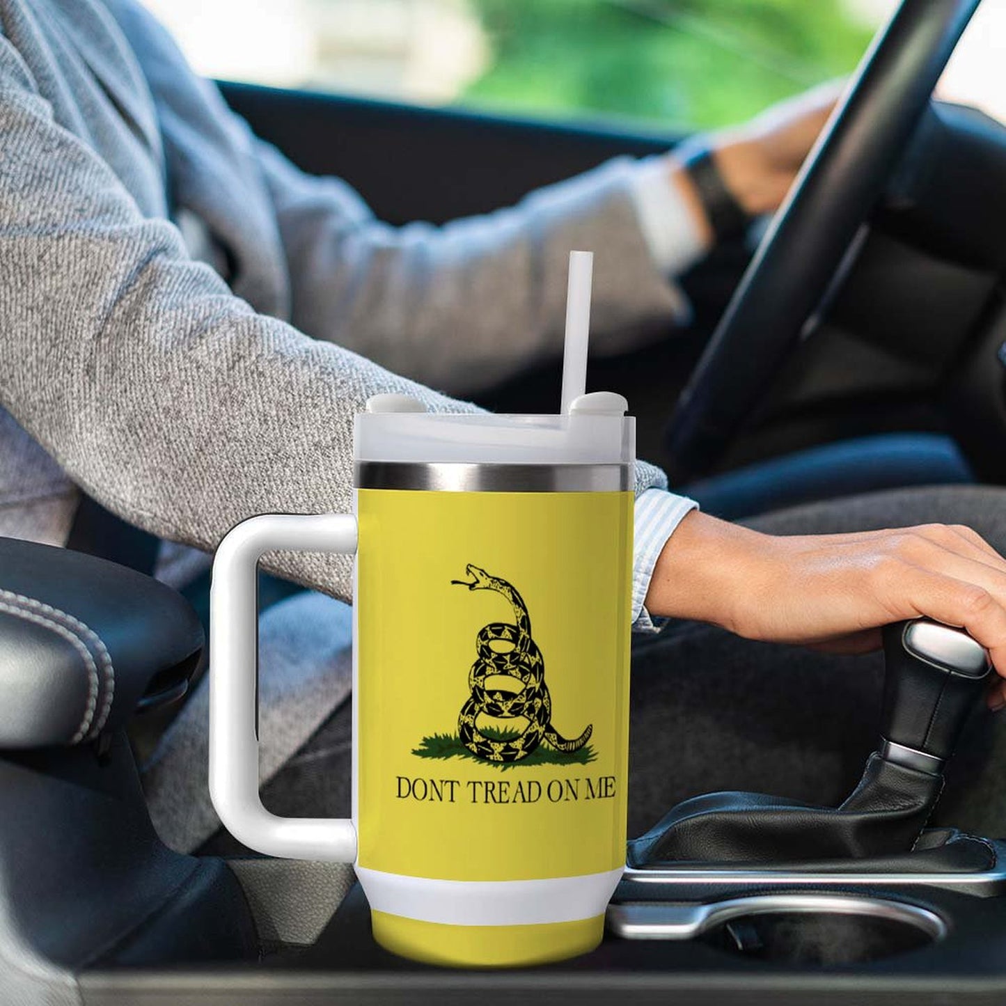 Person driving with [Brand] yellow tumbler featuring snake illustration.