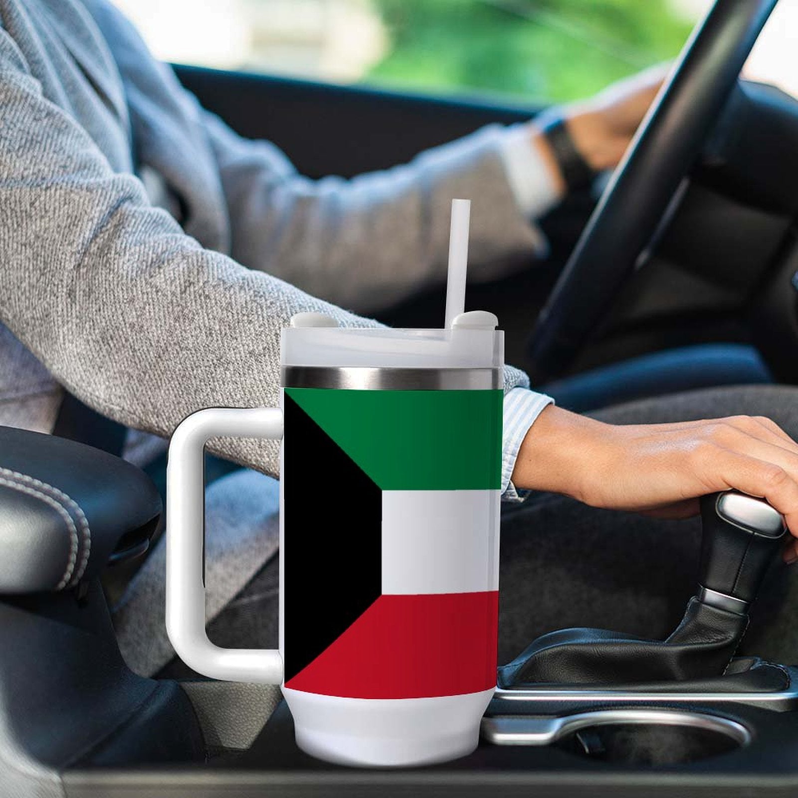 Driver holding gearshift beside [Brand] mug with Kuwaiti flag design.