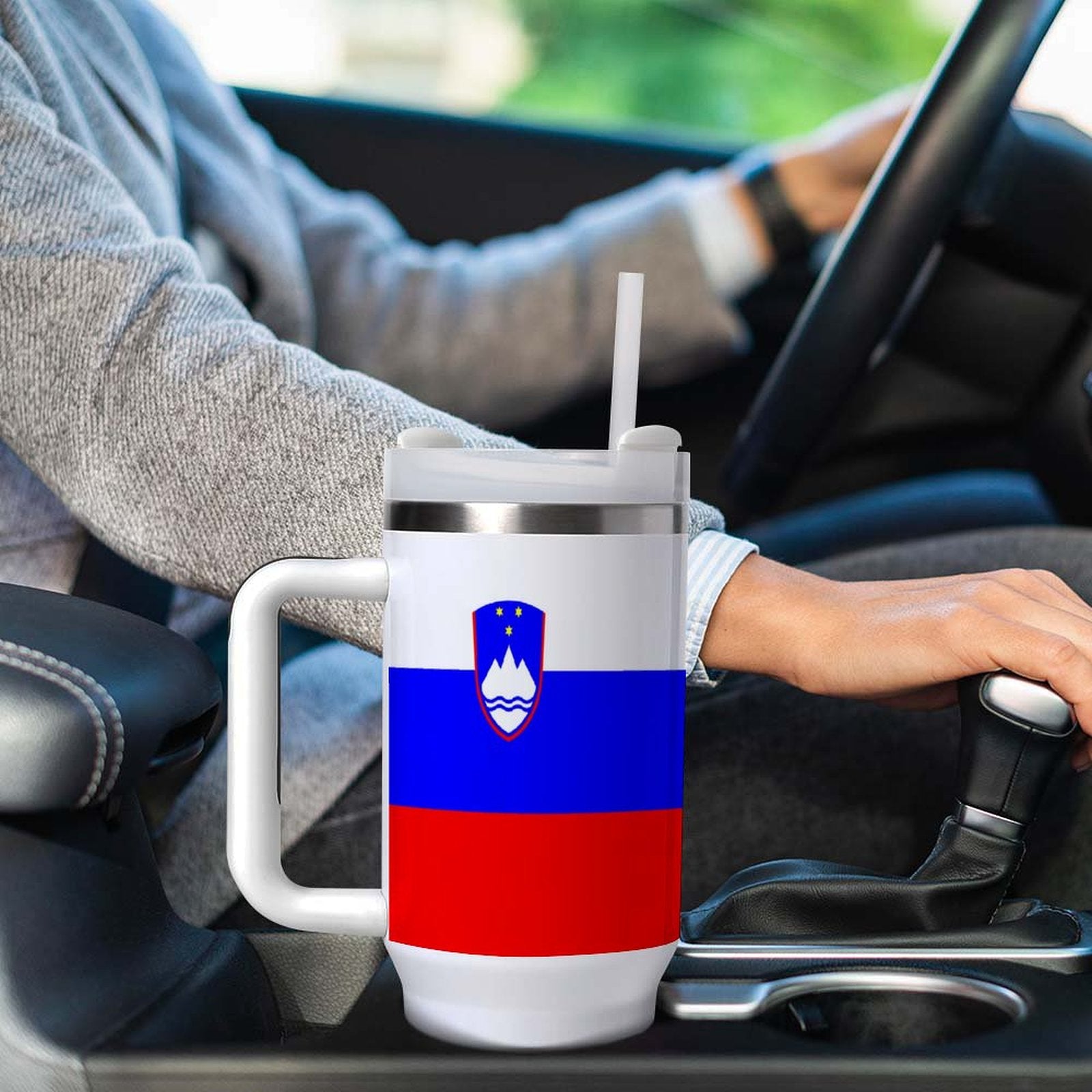 Person driving car with [Brand] Slovenia-themed tumbler.