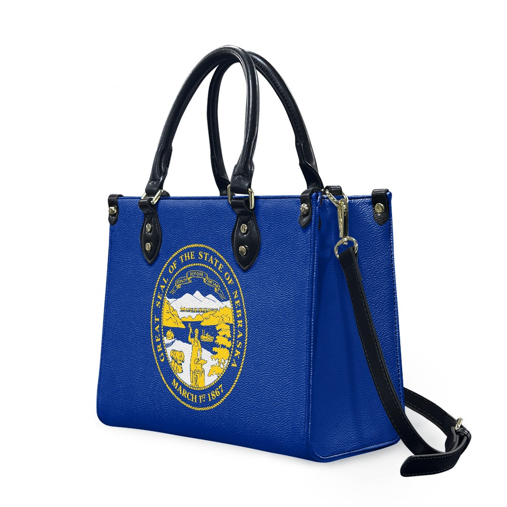 Blue handbag with Nebraska seal, black handles, [Brand] design.
