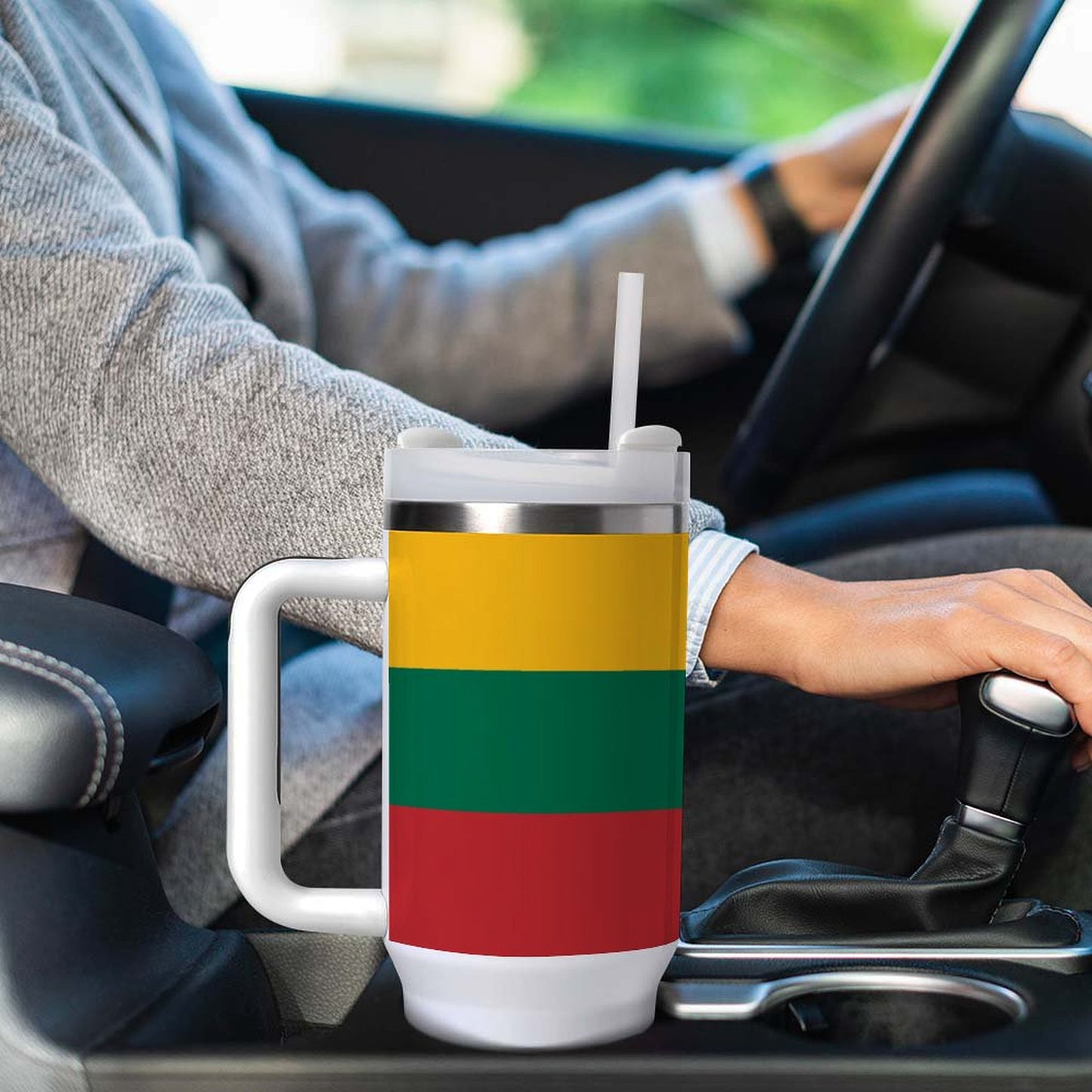 Person driving with [Brand] flag-themed mug in car holder.