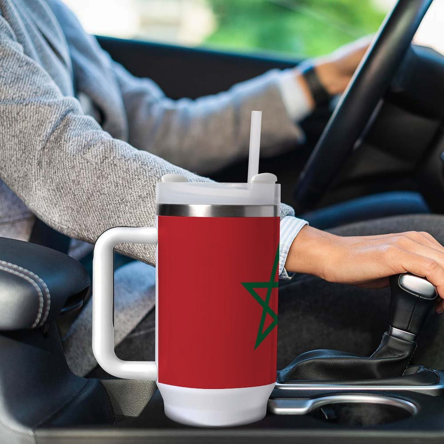 Person driving with [Brand] red travel mug in car.