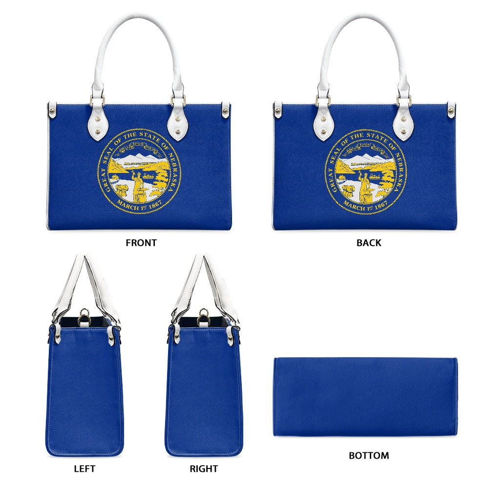 Blue [Brand] handbag featuring Nebraska seal with white handles.