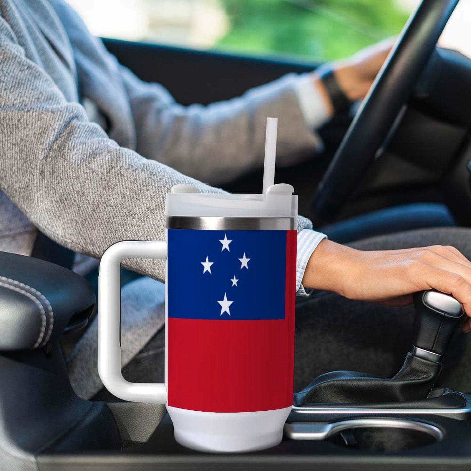 Driver holds [Brand] mug with flag design in car.
