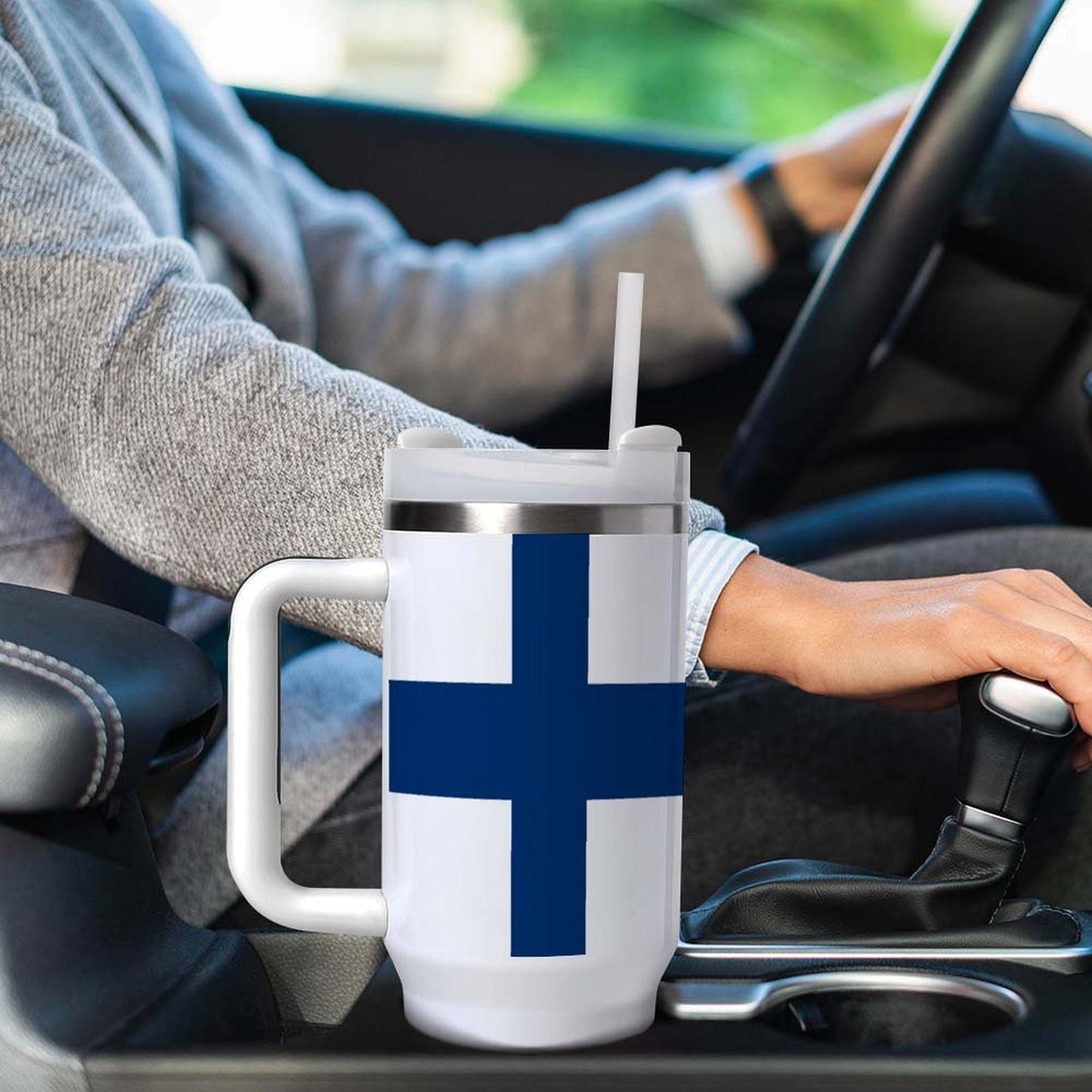 Driver holding gearshift next to [Brand] mug with straw.