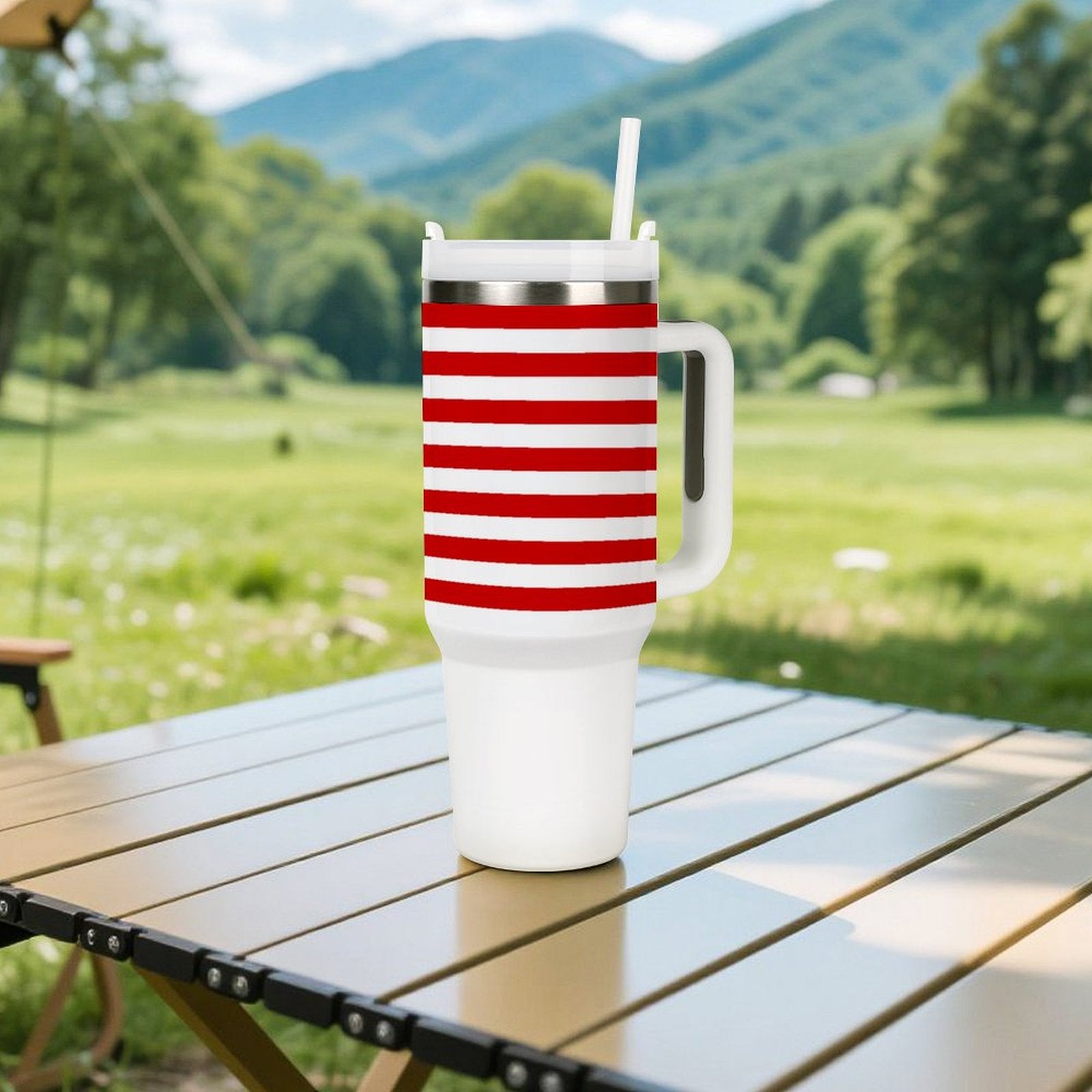 [Brand] striped mug with straw outdoors on table, mountains background.