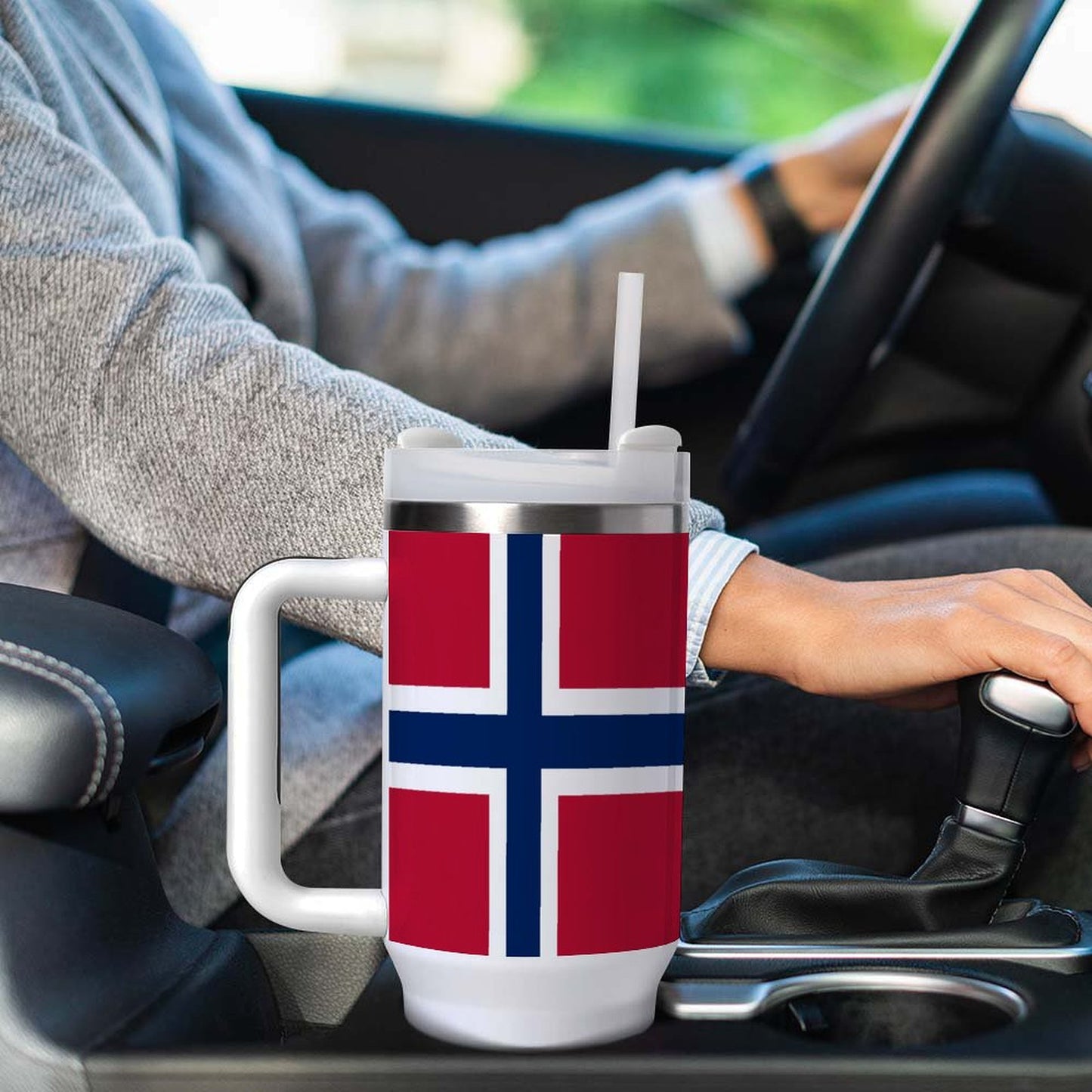 Driver holding [Brand] mug featuring Norwegian flag, inside car.