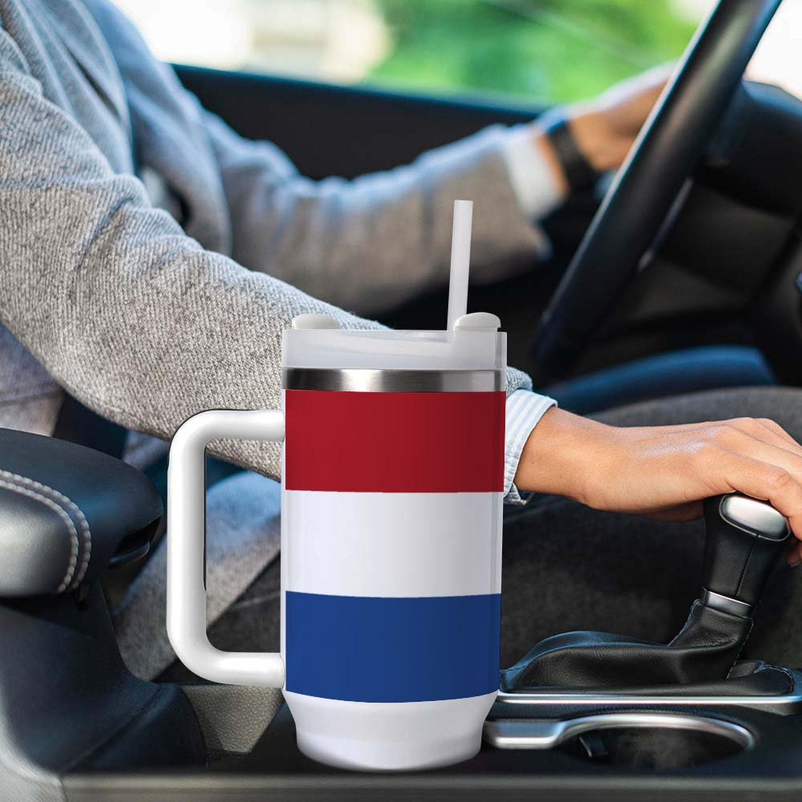 A [Brand] insulated mug in car cup holder, driver steering.