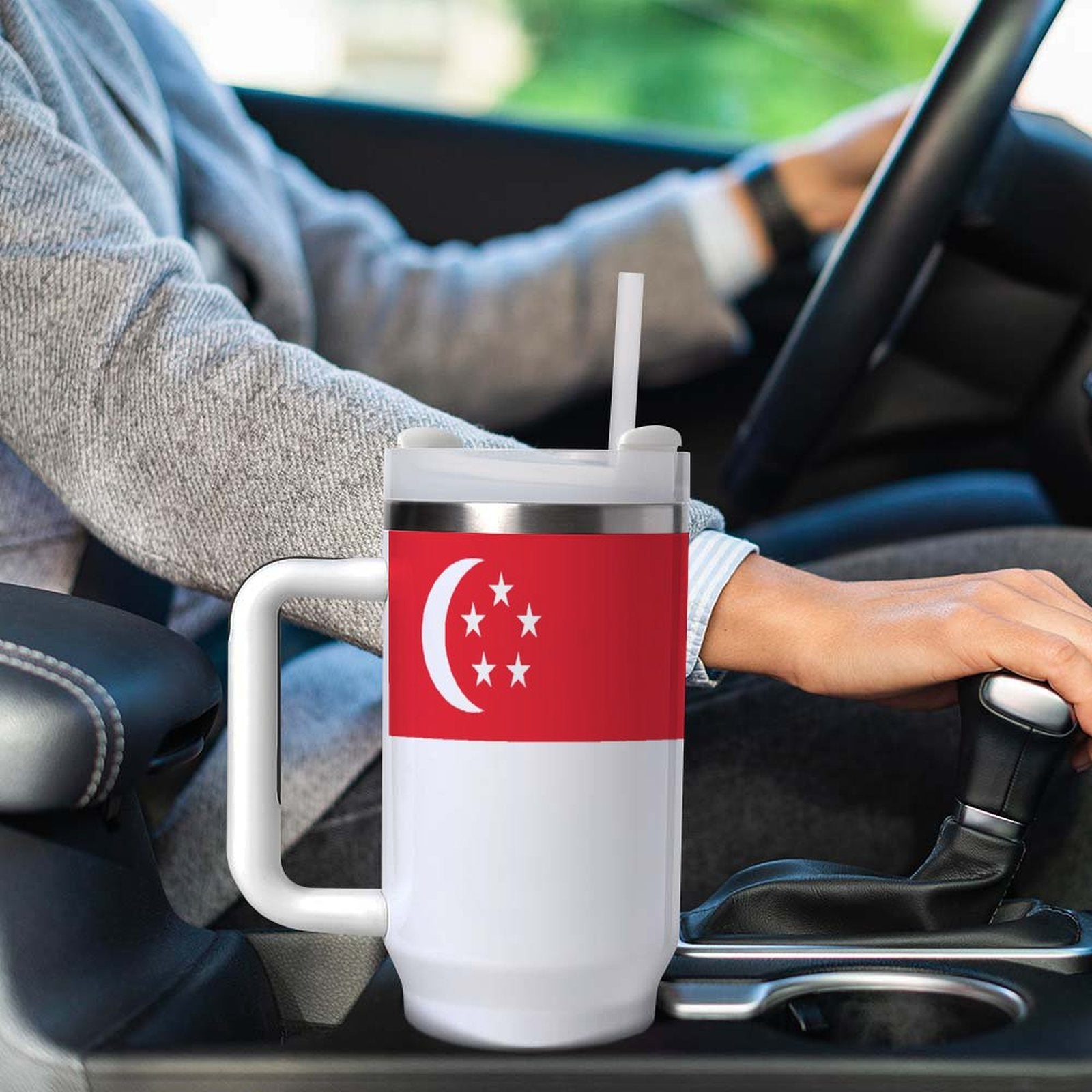 Person driving with [Brand] Singapore flag mug in holder.