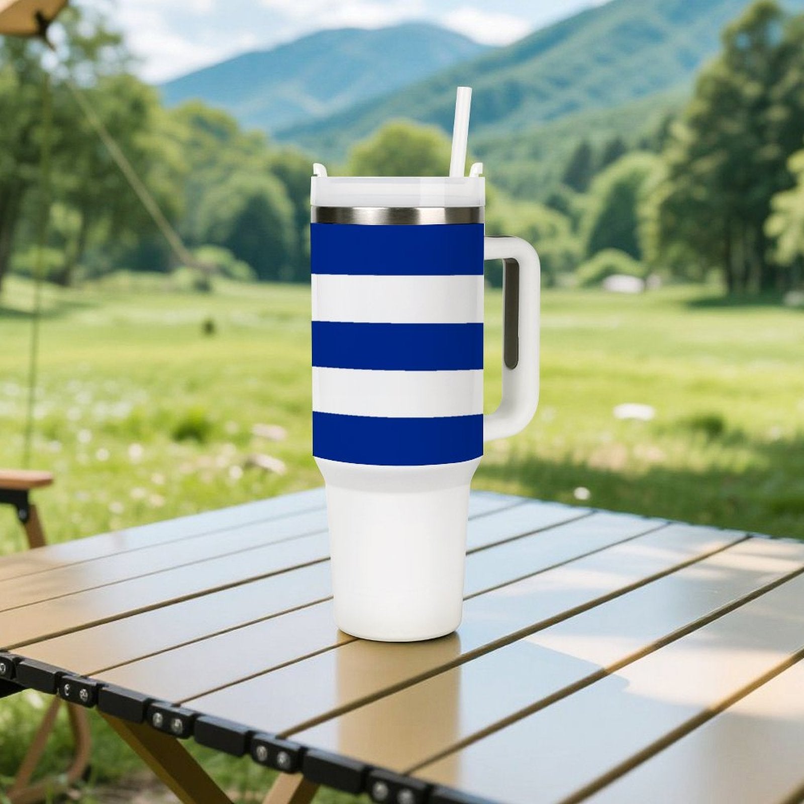 [Brand] striped tumbler with handle on outdoor table, mountains backdrop.