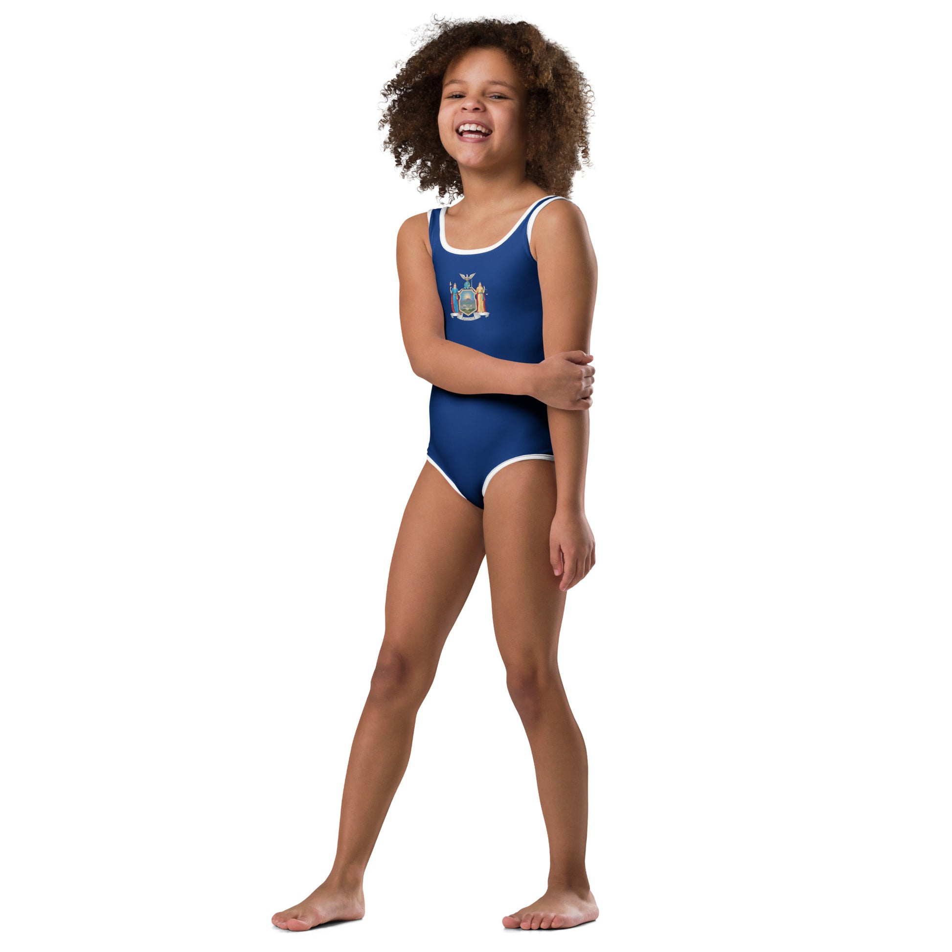 Young girl in [Brand] navy swimsuit, smiling and standing confidently.
