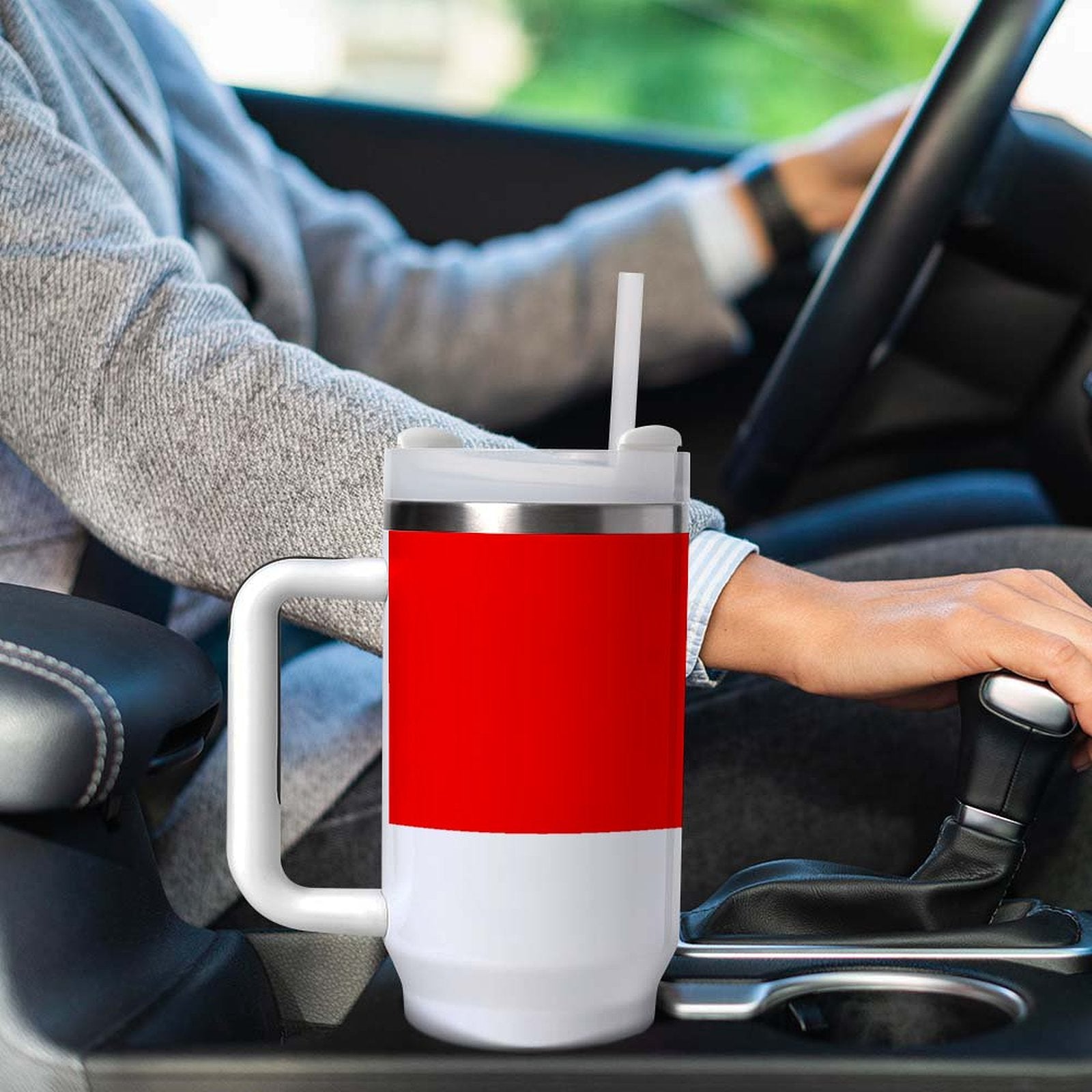 Person drives car with [Brand] red travel mug nearby.