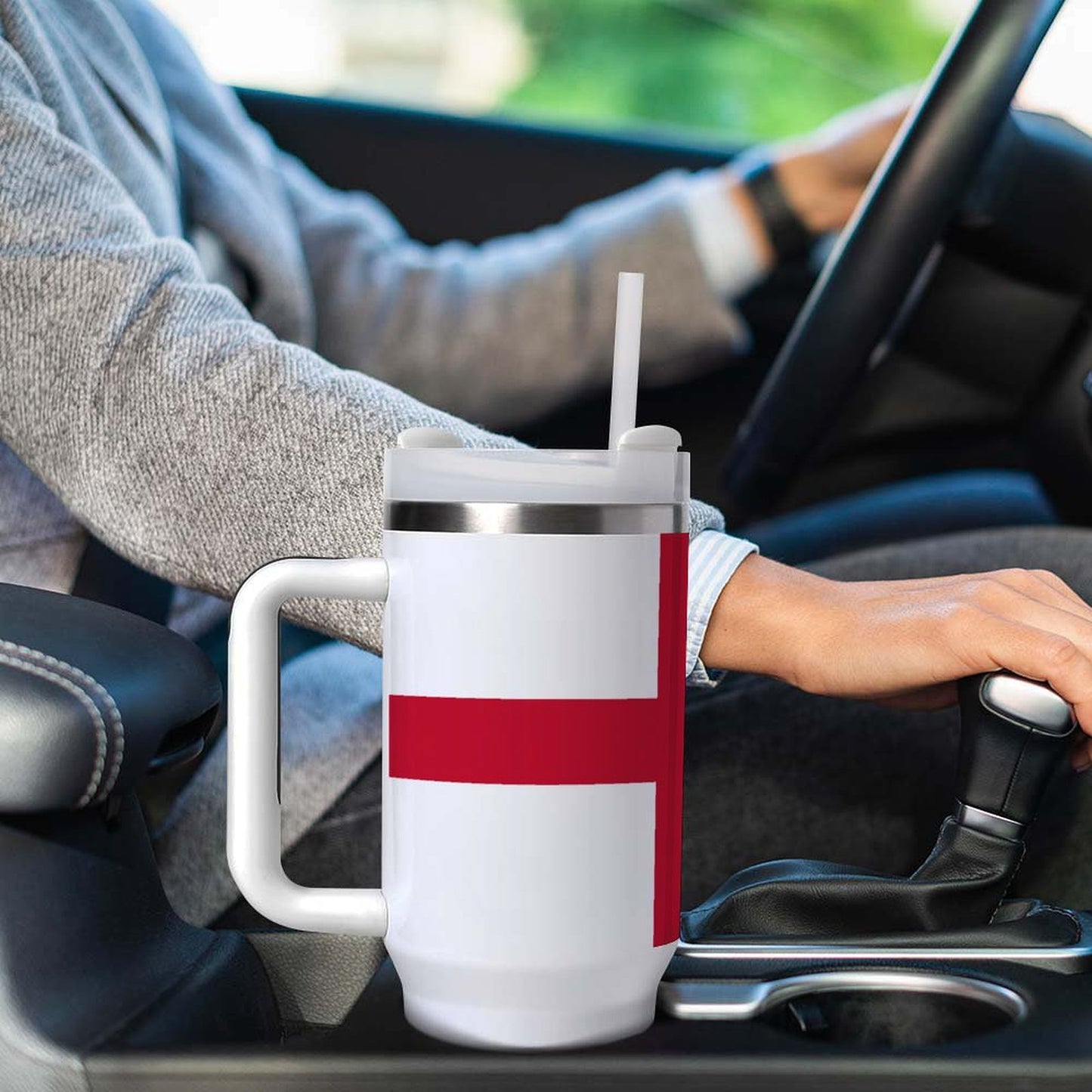 Person driving with [Brand] mug featuring red cross design.