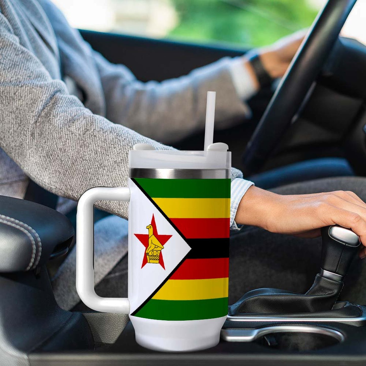 Person driving car with [Brand] Zimbabwean flag travel mug.