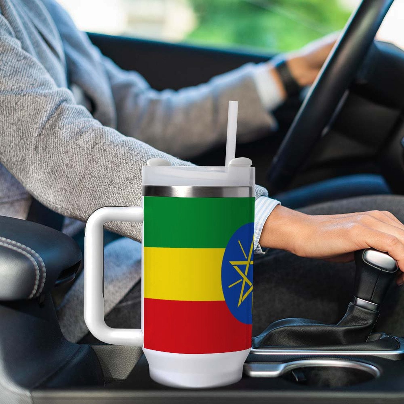 Person driving car with [Brand] Ethiopian flag-themed travel mug.
