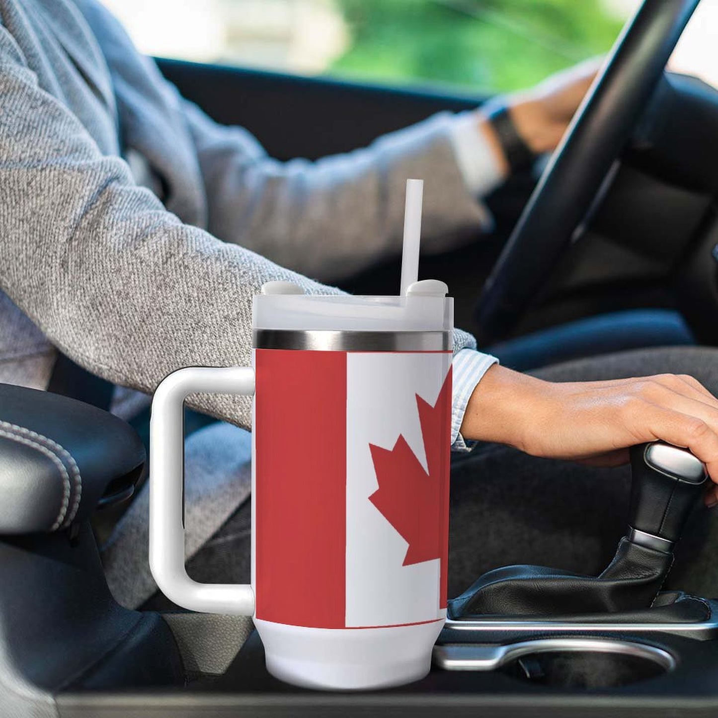 Driver holding steering wheel with [Brand] Canadian flag mug.