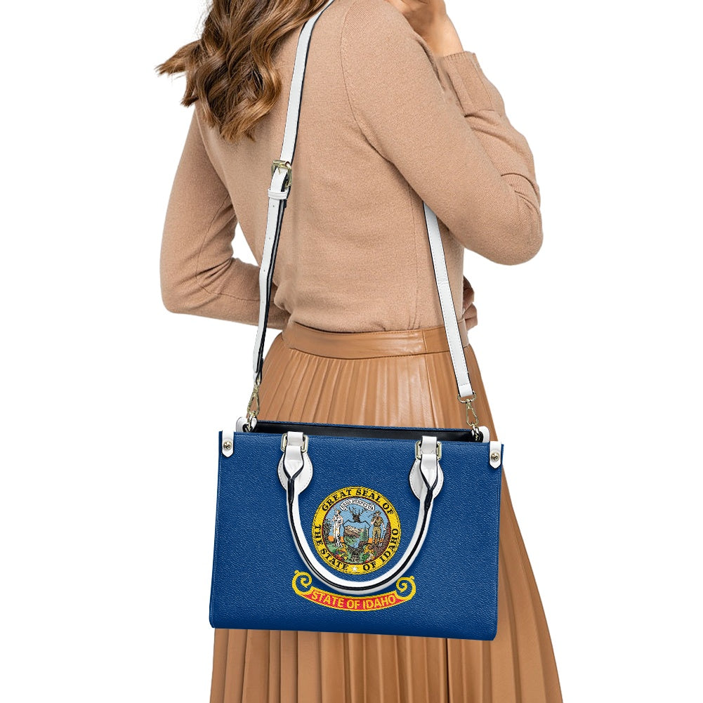 Woman carrying [Brand] blue handbag with Idaho state emblem.