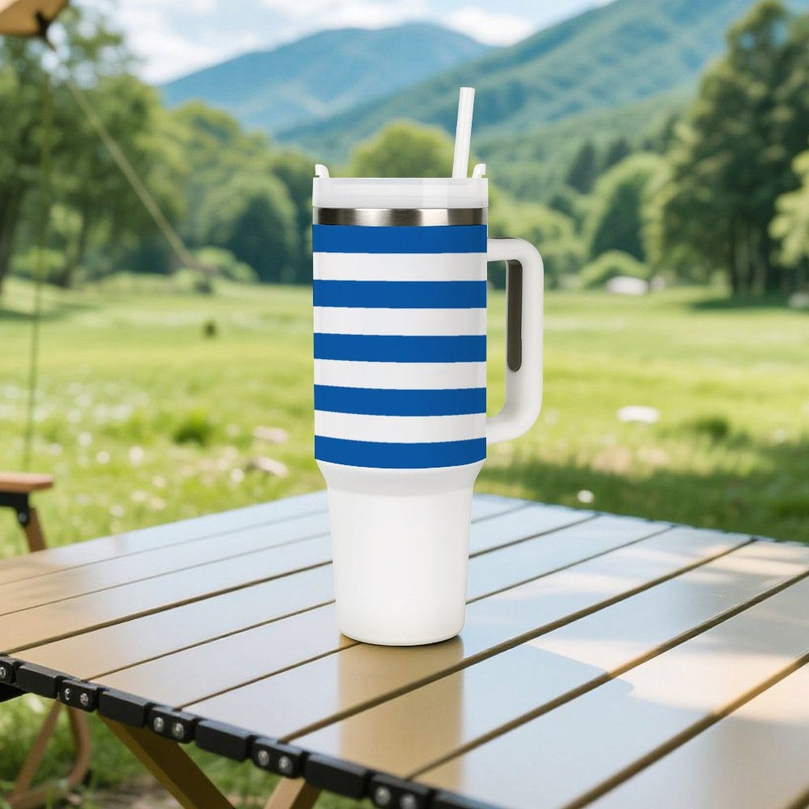 [Brand] striped tumbler on outdoor table, mountains in background.