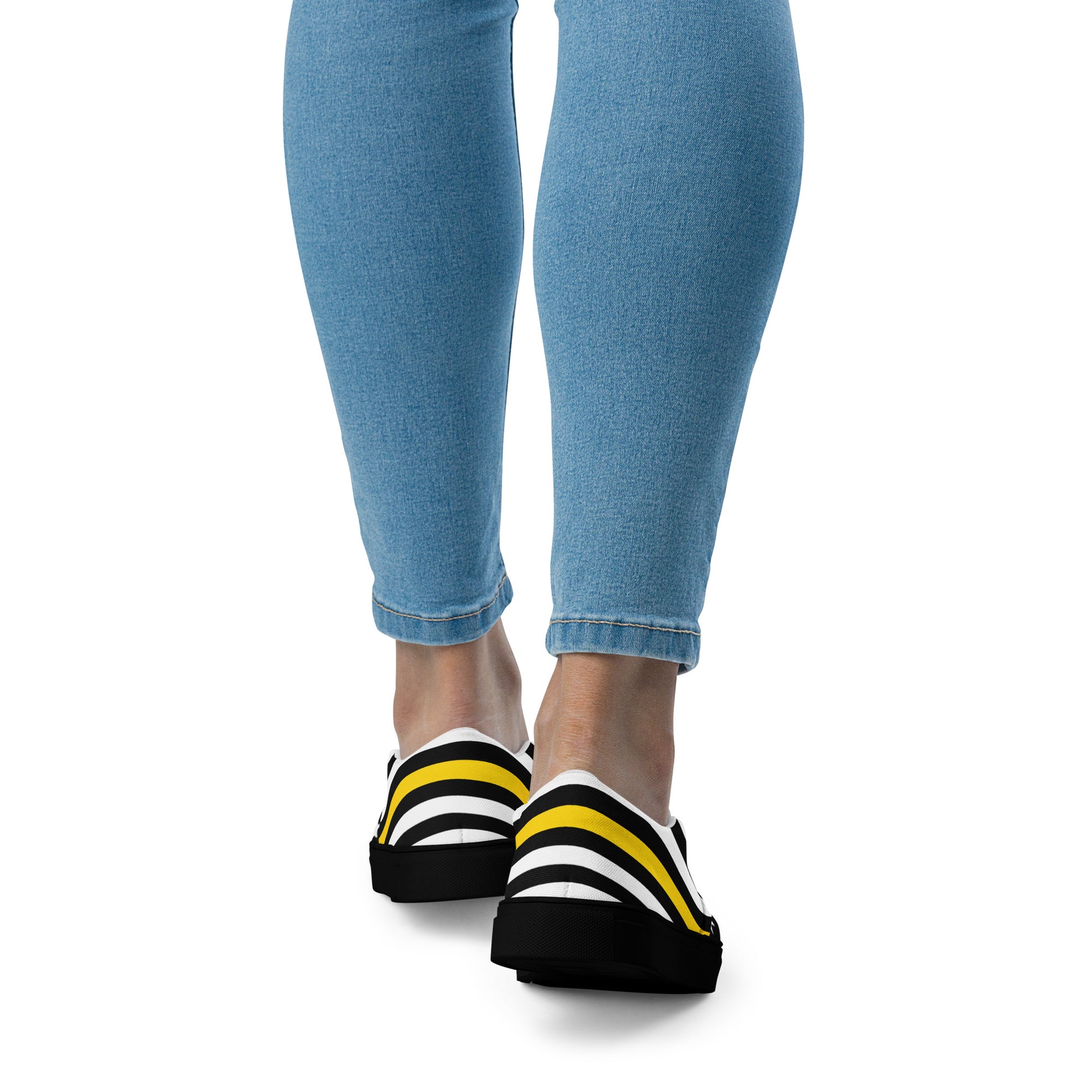 [Brand] sneakers with yellow stripes, worn with blue jeans.